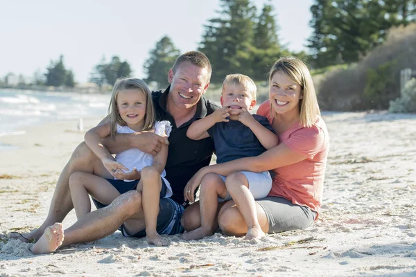 Glada vackra kaukasiska familjen ha semester på stranden leende med mor och far sitter på sand med lilla son och ung dotter — Stockfoto