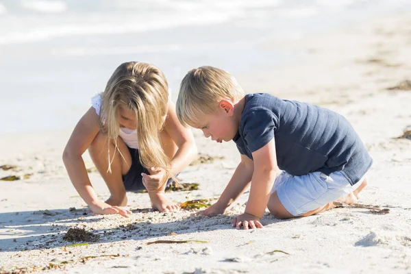 Kleine entzückende und süße Geschwister spielen zusammen im Sandstrand mit kleinem Bruder umarmen und schöne blonde junge Schwester — Stockfoto