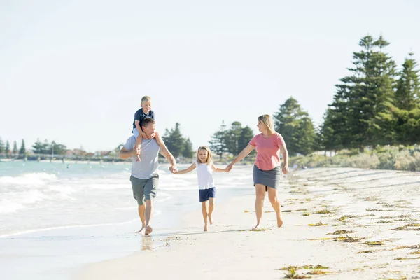 Young happy and beautiful family mother father holding hand of son and daughter walking joyful on the beach enjoying Summer holidays — Stock Photo, Image