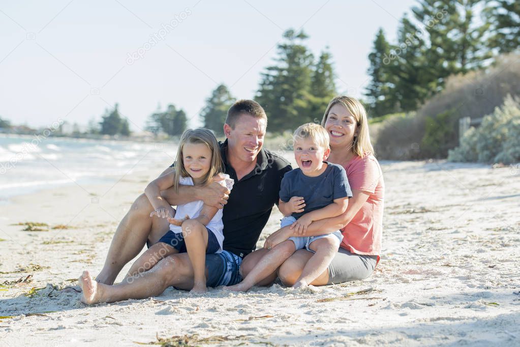 happy beautiful Caucasian family having holidays on the beach smiling with mother and father sitting on sand with little son and young daughter
