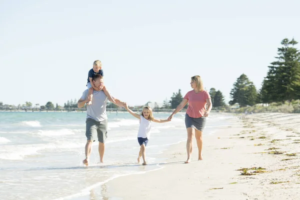Jovem feliz e bonita família mãe pai segurando mão de filho e filha andando alegre na praia desfrutando de férias de verão — Fotografia de Stock