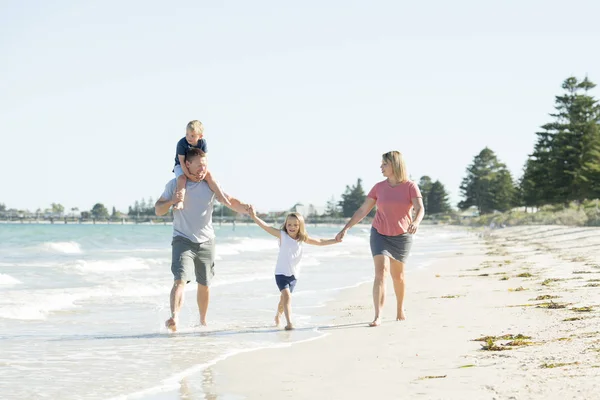 Young happy and beautiful family mother father holding hand of son and daughter walking joyful on the beach enjoying Summer holidays — Stock Photo, Image