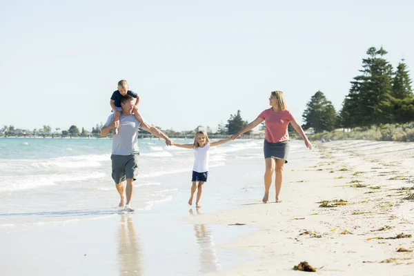 Young happy and beautiful family mother father holding hand of son and daughter walking joyful on the beach enjoying Summer holidays — Stock Photo, Image