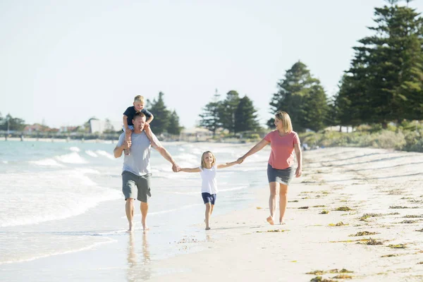 Young happy and beautiful family mother father holding hand of son and daughter walking joyful on the beach enjoying Summer holidays — Stock Photo, Image