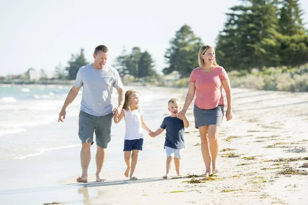 Ayah ibu muda yang bahagia dan cantik bergandengan tangan dari anak laki-laki dan anak perempuan berjalan dengan gembira di pantai menikmati liburan musim panas — Stok Foto