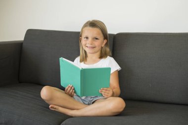 Genç tatlı ve mutlu küçük kız 6 ya da 7 yaşında sessiz ve çocuk eğitiminde çok güzel bir kitap okuma ev oturma odası kanepe kanepede oturan