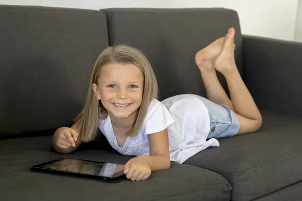 Jovem doce e feliz menina 6 ou 7 anos de idade deitado em casa sala de estar sofá usando internet tablet digital touch pad — Fotografia de Stock