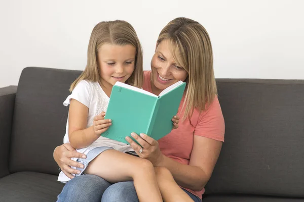 Young beautiful and happy women sitting together with her adorable 7 years old adorable blond girl reading book enjoying telling story — Stock Photo, Image