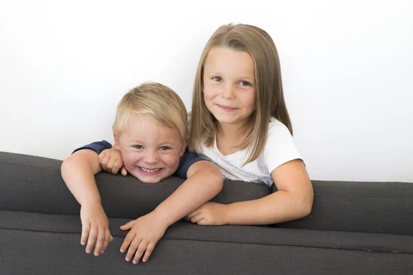 7 years old beautiful little girl posing happy at home sofa couch with her small cute young 3 years old brother in siblings love relationship — Stock Photo, Image