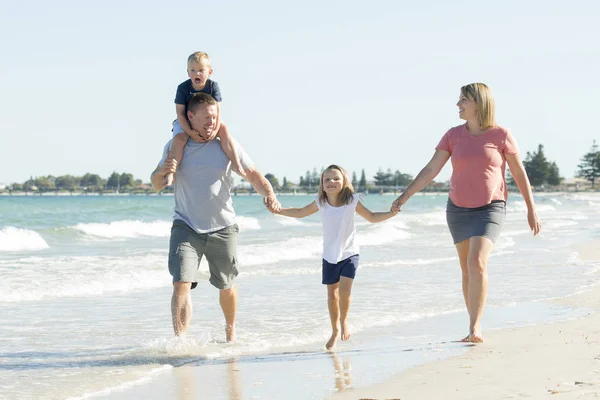 Joven feliz y hermosa familia madre padre de la mano del hijo y la hija caminando alegre en la playa disfrutando de vacaciones de verano — Foto de Stock