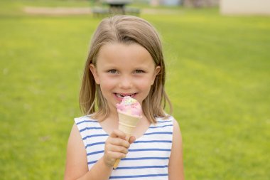 çok güzel ve güzel sarışın genç kız 6 ya da 7 yaşında yeşil çim alan arka plan üzerinde izole lezzetli dondurma mutlu gülümseyerek yeme 