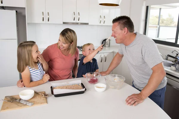 Young happy couple baking together with little son and young beautiful daughter at home kitchen having fun playing with cream — Stock Photo, Image