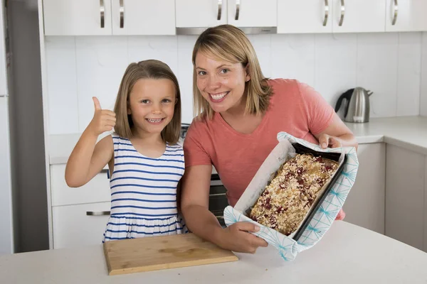 母亲和她甜美的美丽的7岁的女儿给拇指显示骄傲的草莓蛋糕后, 一起在家里的厨房烘烤 — 图库照片