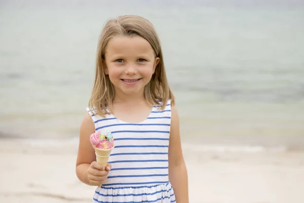 Retrato de adorable y hermosa joven rubia de 6 o 7 años comiendo delicioso helado sonriendo feliz aislado en el fondo de la playa de mar — Foto de Stock