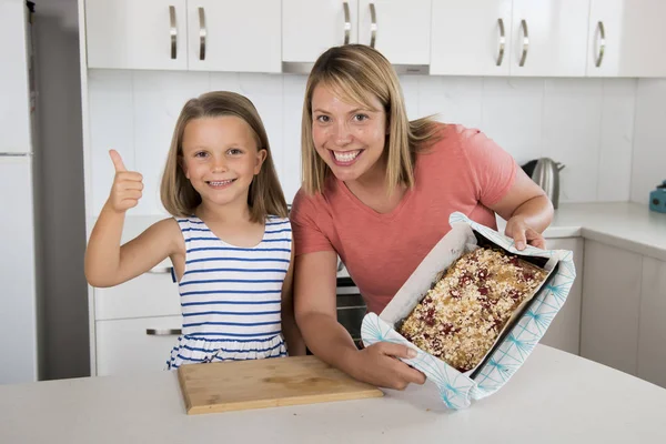 母亲和她甜美的美丽的7岁的女儿给拇指显示骄傲的草莓蛋糕后, 一起在家里的厨房烘烤 — 图库照片