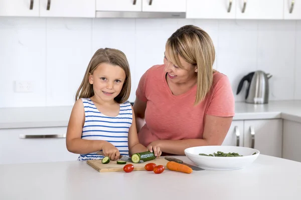 Giovane donna attraente cucinare insieme con la sua dolce bella bionda piccola 6 o 7 anni figlia sorridente felice preparazione insalata — Foto Stock