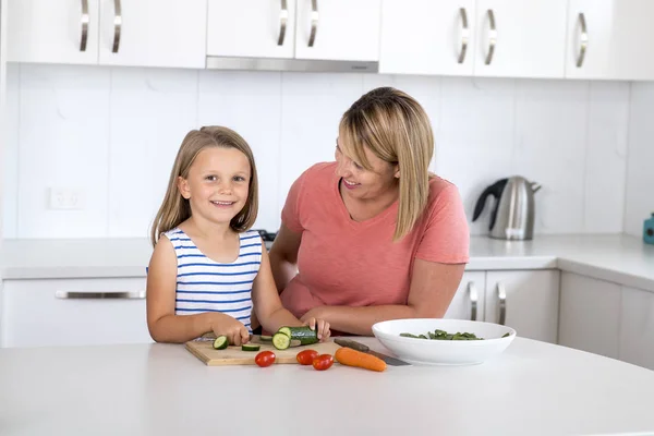 年轻漂亮的女人一起做饭与她甜美的美丽的金发小6或7岁的女儿笑着高兴准备沙拉 — 图库照片