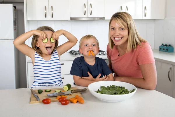 年轻漂亮的女人一起做饭与小3和7岁的儿子和女儿玩黄瓜棒作为眼睛准备沙拉的快乐 — 图库照片