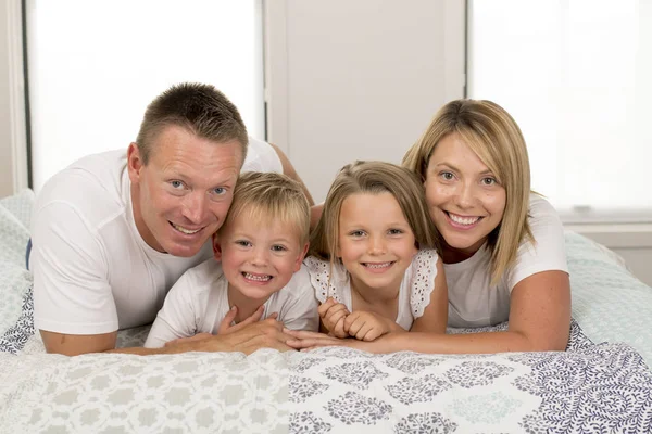 Giovane bella e radiosa coppia 30-40 anni sorridente felice posa dolce sdraiato sul letto con piccolo figlio e bella figlia a casa — Foto Stock