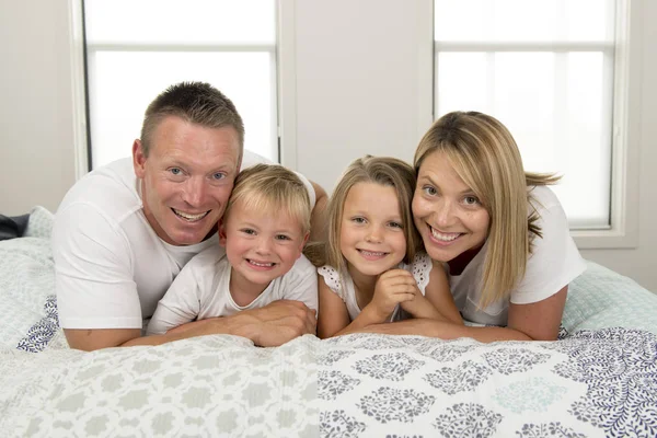 Young beautiful and radiant couple 30 to 40 years old smiling happy posing sweet lying on bed with little son and beautiful daughter at home — Stock Photo, Image