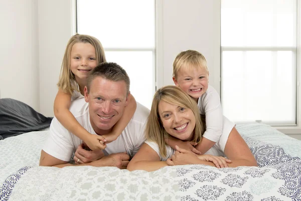 Jovem casal bonito e radiante 30 a 40 anos sorrindo feliz posando doce deitado na cama com pequeno filho e bela filha em casa — Fotografia de Stock