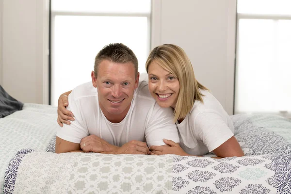 Belo e radiante casal sorrindo feliz posando doce deitado na cama em casa no conceito de relacionamento bem sucedido marido esposa — Fotografia de Stock