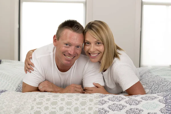 Jovem casal romântico bonito e radiante 30 a 40 anos sorrindo feliz no amor posando doce e abraço deitado na cama em casa quarto — Fotografia de Stock