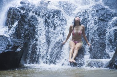 genç güzel ve tatlı Asyalı kadın vücut akışı rock duygu saflık üzerinde oturan doğal inanılmaz şelale altında ıslak bikini