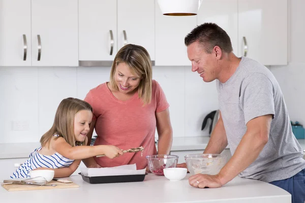 Jovem casal feliz cozimento em conjunto com pequena filha bonita em casa cozinha se divertindo brincando com creme no estilo de vida familiar — Fotografia de Stock