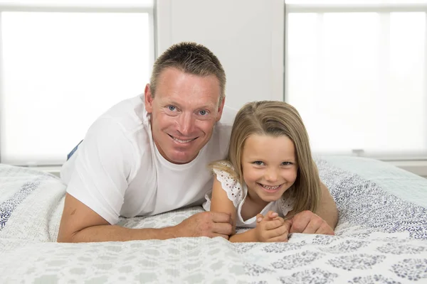 Giovane uomo sdraiato sul letto insieme con adorabile bambina di 7 anni che gioca felice a casa in famiglia padre e figlia amano il concetto di stile di vita — Foto Stock