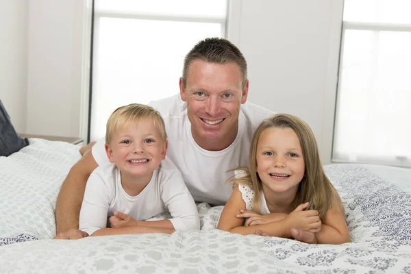 Junger Mann liegt auf dem Bett zusammen mit ihrem kleinen süßen 3 und 7 Jahre alten Sohn und Tochter spielen glücklich in Familie Vater Kinder lieben Lebensstil — Stockfoto