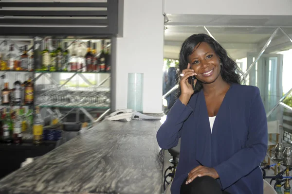 Mooie zwarte Afro Amerikaanse zakenvrouw op haar 30s zit op resort restaurant bar praten op mobiele telefoon — Stockfoto