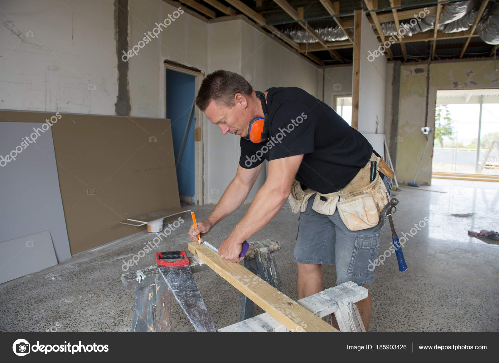 Attractive and confident constructor carpenter or builder man working measuring wood with manual saw at industrial construction site in installation and ...