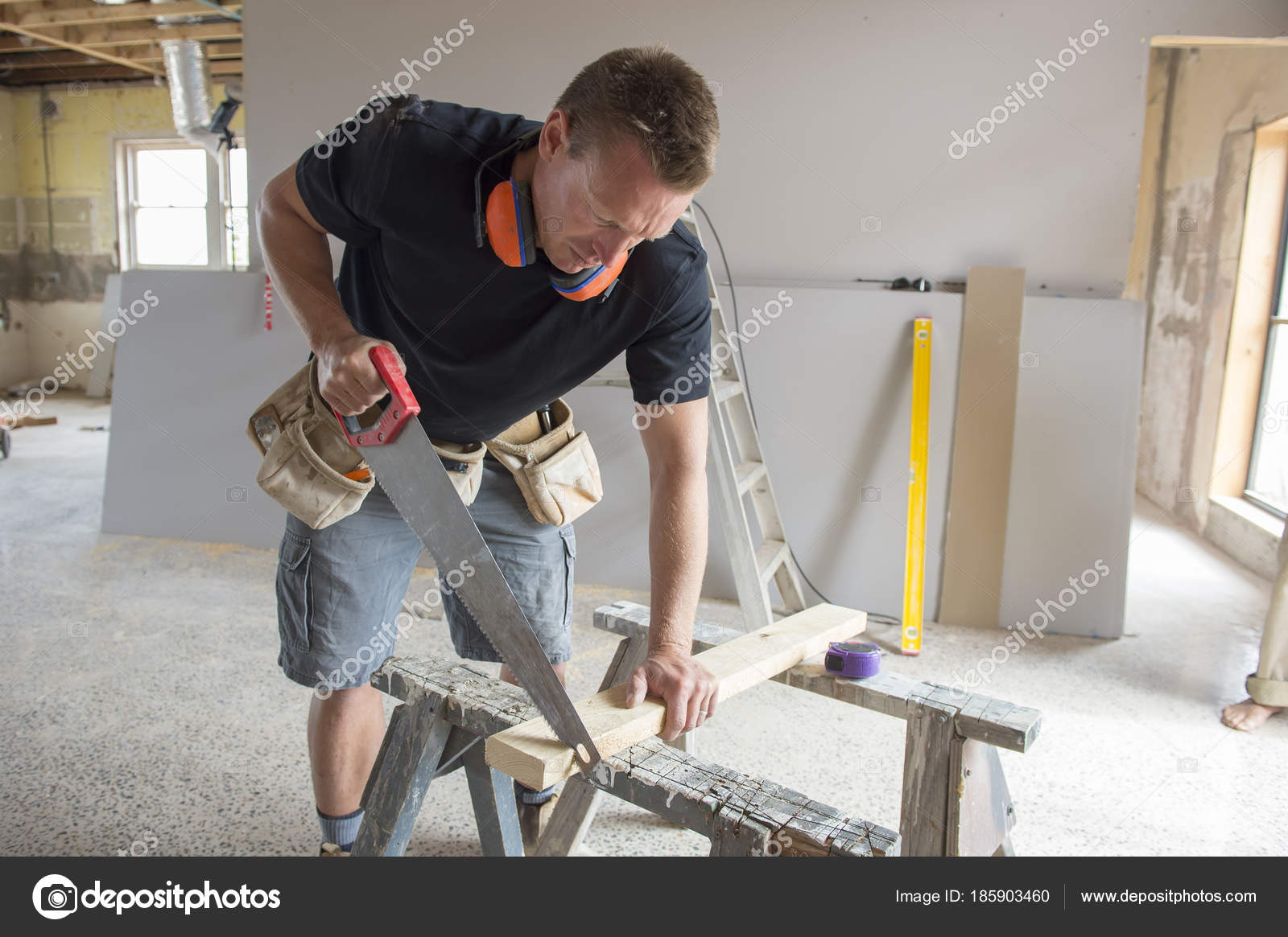 Attractive and confident constructor carpenter or builder man working cutting wood with manual saw at industrial construction site in installation and ...