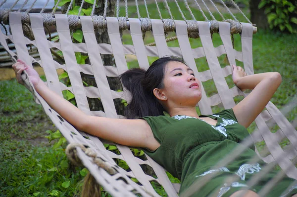 Sweet and relaxed Asian Chinese woman on her 20s wearing green Summer dress lying thoughtful pensive and comfortable in beautiful hammock — Stock Photo, Image