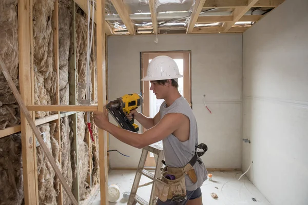 Jeune stagiaire de l'industrie du bâtiment âgé d'une vingtaine d'années portant un casque de protection apprenant à travailler avec une perceuse sur le site d'un atelier industriel — Photo