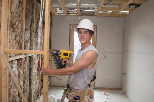 Jeune stagiaire de l'industrie du bâtiment âgé d'une vingtaine d'années portant un casque de protection apprenant à travailler avec une perceuse sur le site d'un atelier industriel — Photo