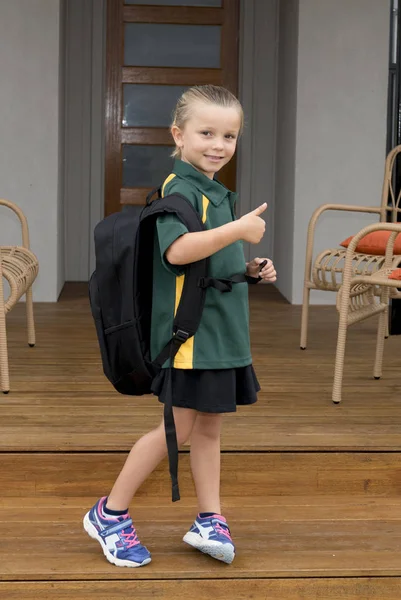 6 eller 7 år gamla flickebarn som ler lyckligt leende glada transporterar stora tunga skola ryggsäck bär ung flicka student uniform — Stockfoto