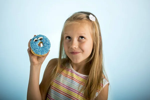 Jeune belle fille blonde heureuse et excitée 8 ou 9 ans tenant beignet désert sur sa main regardant spastique et joyeux dans l'abus de sucre et la dépendance — Photo