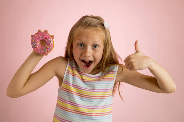 Jeune belle fille blonde heureuse et excitée 8 ou 9 ans tenant beignet désert sur sa main regardant spastique et joyeux dans l'abus de sucre et la dépendance — Photo