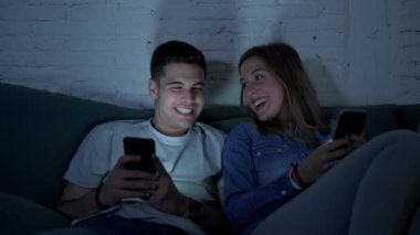 Genç mutlu ve romantik çift birlikte istimal hareket eden telefon oturma zevk onların 20s üzerinde tarama ve eğlenmek internet uygulaması ile internet bağımlılığı kavramında koltuk kanepe Anasayfa