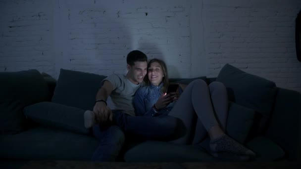 年轻快乐和浪漫的情侣在他们的20S 一起使用手机享受坐在家里沙发沙发浏览和玩网络成瘾的互联网应用的乐趣的概念 — 图库视频影像