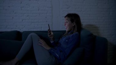 Genç mutlu genç kız ya da kadın üzerinde ev kanepeye geç gece cep telefonunda videocall zevk ve iletişim teknoloji bağımlılığı kavramı içinde app dating internet sosyal medya kullanarak gülümseyen mutlu yalan 20'li