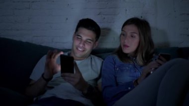 Genç mutlu ve romantik çift birlikte istimal hareket eden telefon oturma zevk onların 20s üzerinde tarama ve Internet app iletişim teknolojisi ve akıllı telefon bağımlılık kavramı ile eğleniyor koltuk kanepe Anasayfa