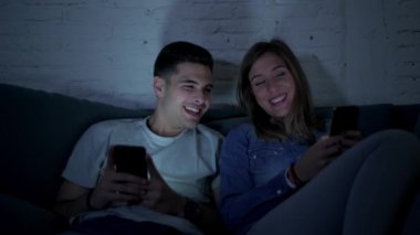 Genç mutlu ve romantik çift birlikte istimal hareket eden telefon oturma zevk onların 20s üzerinde tarama ve Internet app iletişim teknolojisi ve akıllı telefon bağımlılık kavramı ile eğleniyor koltuk kanepe Anasayfa