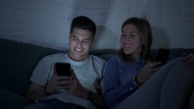 Genç mutlu ve romantik çift birlikte istimal hareket eden telefon oturma zevk onların 20s üzerinde tarama ve Internet app iletişim teknolojisi ve akıllı telefon bağımlılık kavramı ile eğleniyor koltuk kanepe Anasayfa