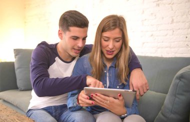 Dijital tablet pad bilgisayarla evde kanepe oturma odası internet mutlu gülümseyerek üzerinde öğeleri seçme satırındaki alışveriş oturan 20'li yaşlarda genç güzel Çift 
