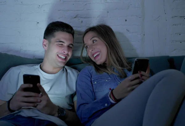 Jeune couple attrayant et heureux en utilisant l'application Internet sur téléphone mobile profiter et rire ensemble assis à la maison canapé salon — Photo