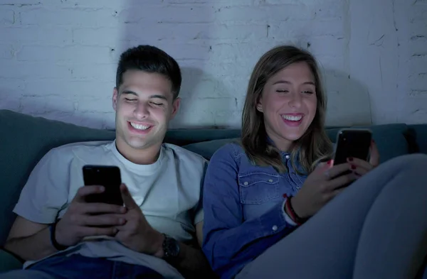 Jeune couple attrayant et heureux en utilisant l'application Internet sur téléphone mobile profiter et rire ensemble assis à la maison canapé salon — Photo