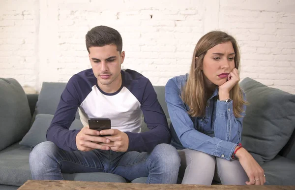 Young attractive couple in relationship problem with internet mobile phone addiction boyfriend ignoring sad neglected and worried girlfriend at home — Stock Photo, Image